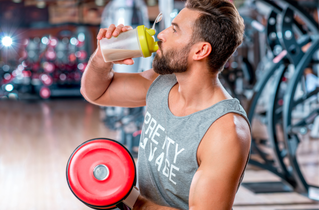 Wie viele Proteinshakes braucht man dargestellt von Muskelmann im Fitnessstudio mit Shake