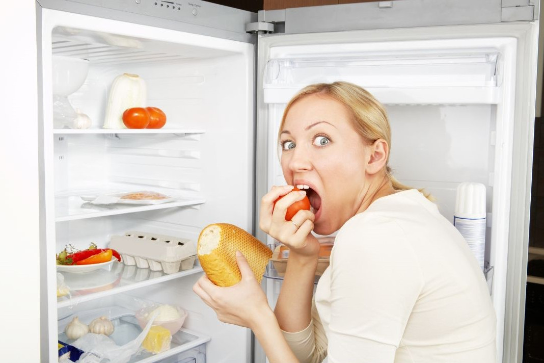 Ghrelin das Hunterhormon symbolisiert von übergewichtiger Frau am Kühlschrank