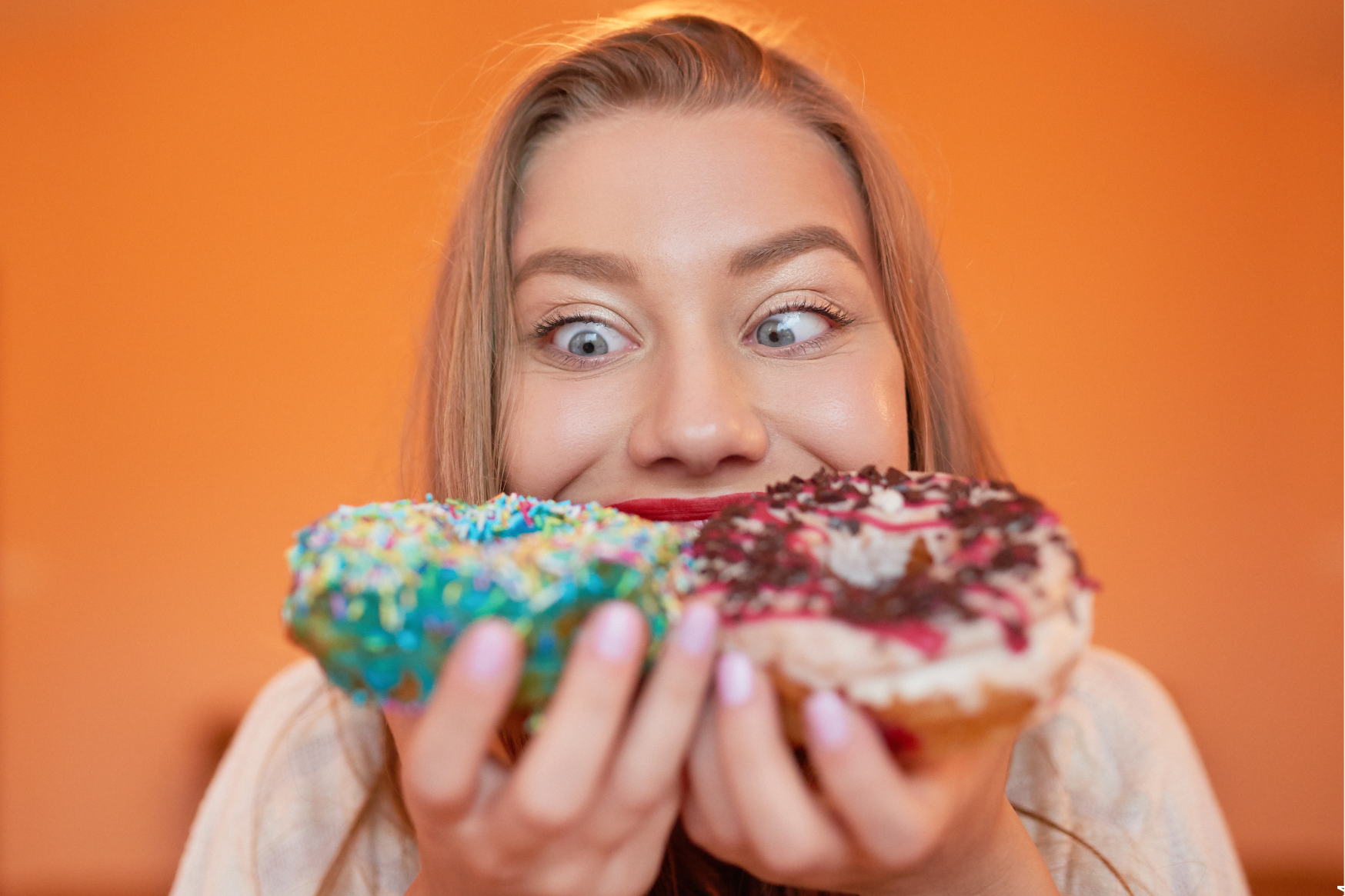 Heißhungerattacken symbolisiert von Frau mit Donats vor dem Mund