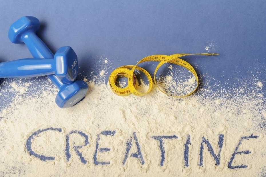 Kreatin dargestellt von Pulver mit Schriftzug, Hantel und Maßband